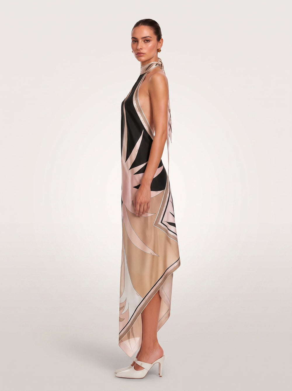 A model wears a sleeveless halter-neck midi dress featuring an abstract yin-yang style print in black, beige, and white, paired with white pointed-toe flats against a light gray studio background.